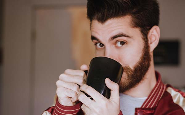 A man in a sports jacket drinking from a mug